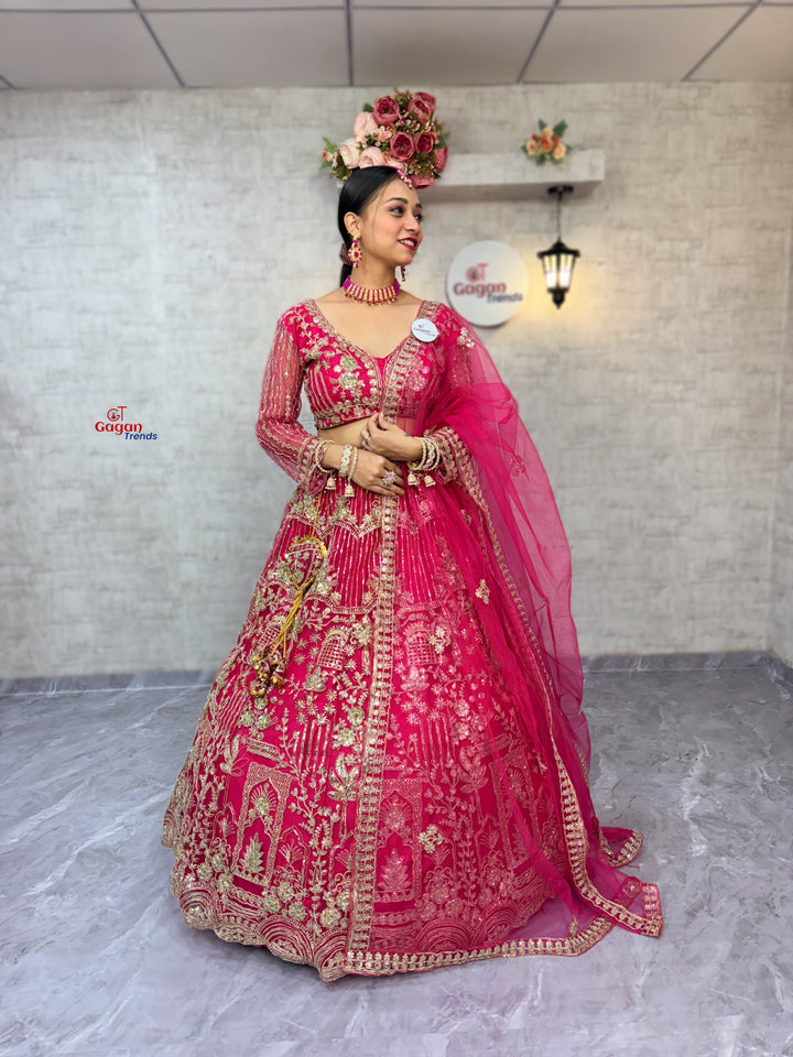 Woman in a traditional pink and gold embroidered outfit standing against a plain background.